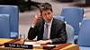 Sam Altman sits at a meeting table beside a nameplate, holding a phone near his ear.